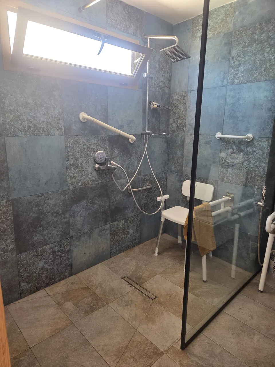 Douche de plain-pied de la salle de bain adaptée, avec paroi vitrée, barres d’appui et siège de douche