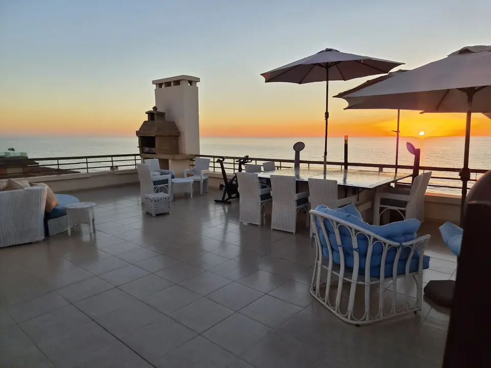 Vue d’ensemble de la grande terrasse au coucher du soleil avec barbecue, salon et salle à manger d’extérieur