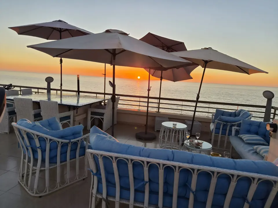Salon et salle à manger d’extérieur sur la terrasse, vue sur la mer au coucher du soleil