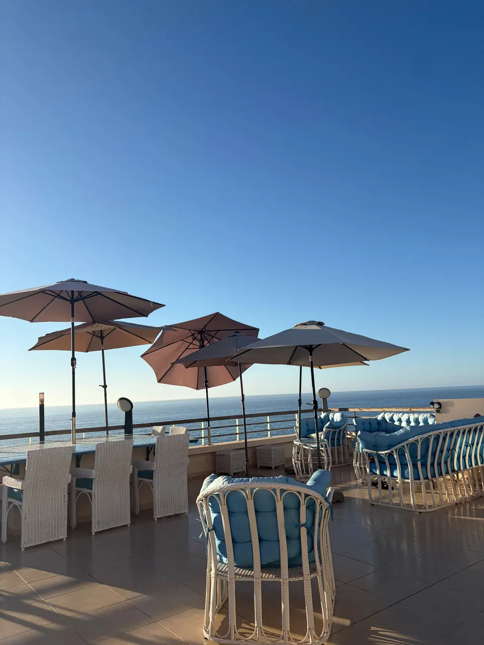 Grande terrasse en journée : parasols, salle à manger d’extérieur et salon face à la mer
